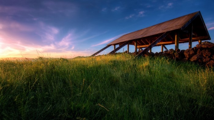 Wooden shelter on a grassy hill at sunset