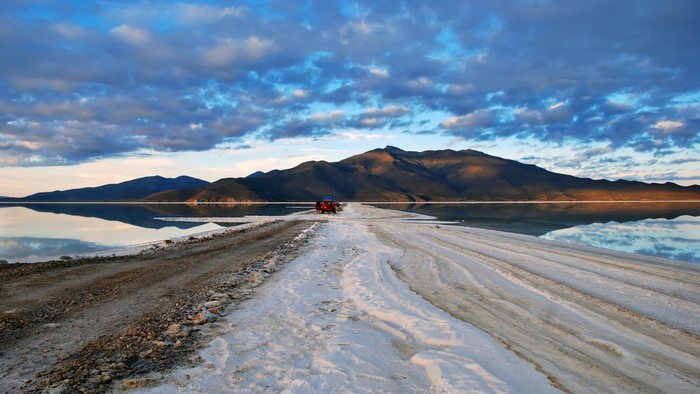 Red vehicle on a salt flat with mountains and clouds