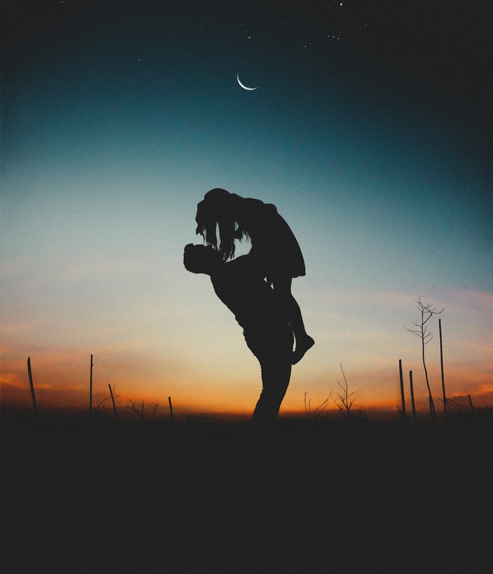 Couple silhouetted against sunset with crescent moon