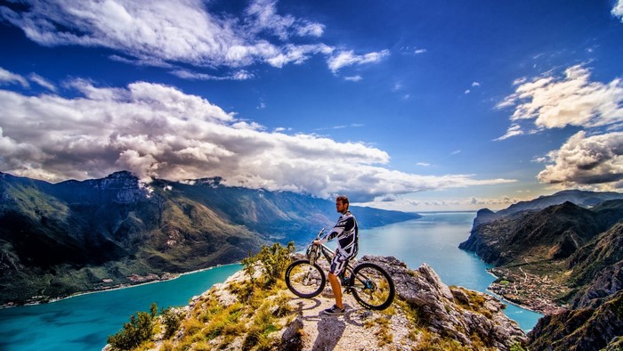 Man with mountain bike on a cliff overlooking a lake
