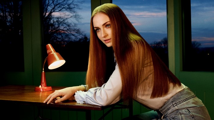 Sophie Turner sitting at a desk with a lamp