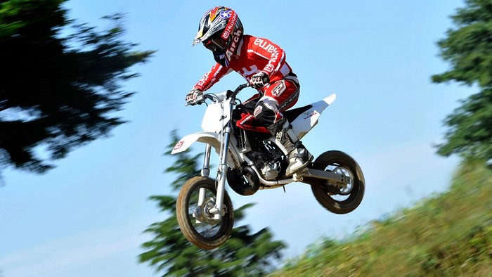 Motocross rider in red gear jumping on a white bike