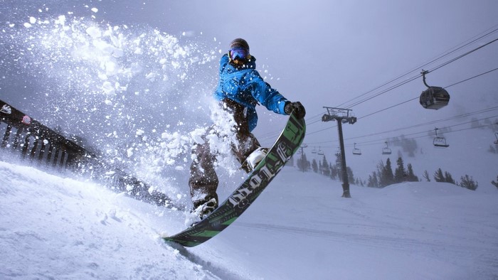 Snowboarder jumping with snow spray and ski lift