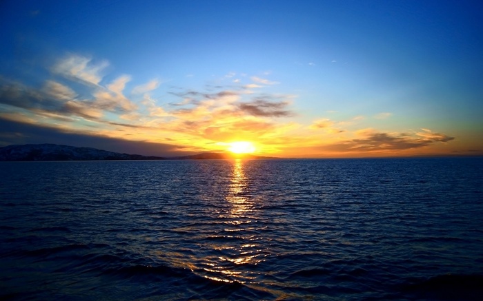 Sunset over the ocean with clouds and mountains
