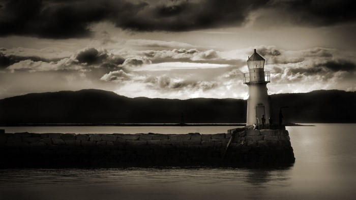 Sepia lighthouse on a stone pier under a cloudy sky