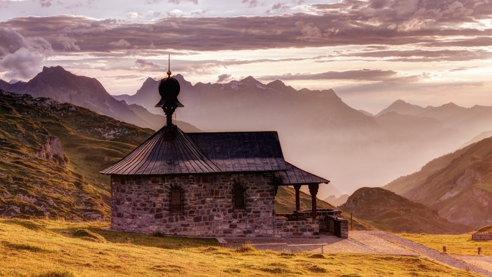 Stone chapel on a grassy mountain slope at sunset