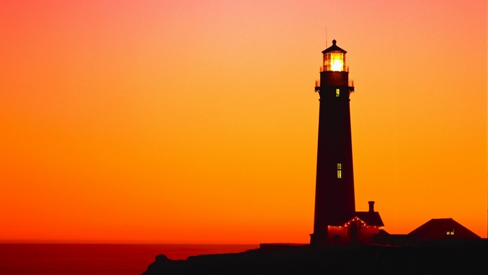 Lighthouse silhouette against a vibrant sunset