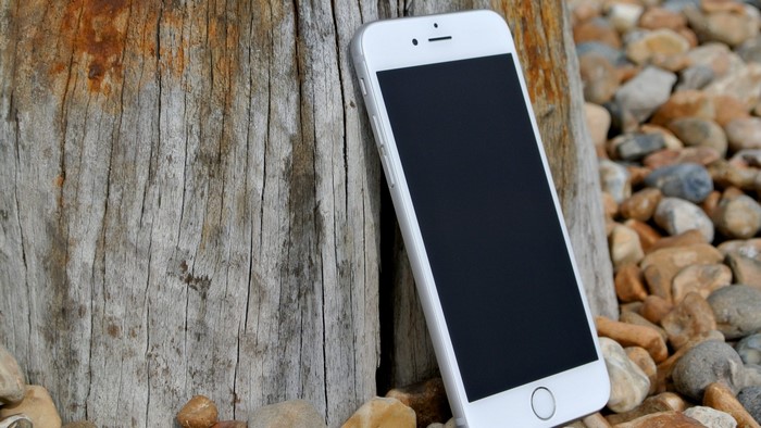 White iPhone leaning against a wooden post with rocks