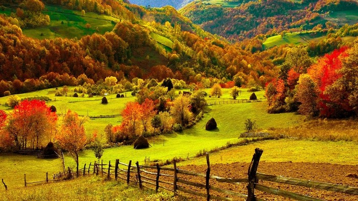 Autumn mountain landscape with haystacks and wooden fence