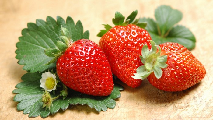 Three ripe strawberries with green leaves and a flower