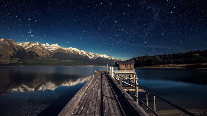 Wooden Pier Under Starry Night Sky with Snow-Capped Mountains