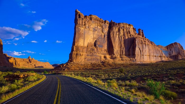 Desert Road Leading to Rock Formations Under Blue Sky