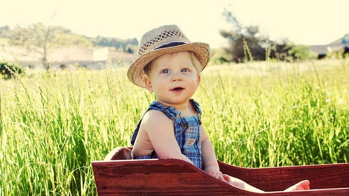 Cute Baby Boy in Overalls and Hat in Field