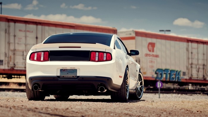 White Ford Mustang parked near train cars