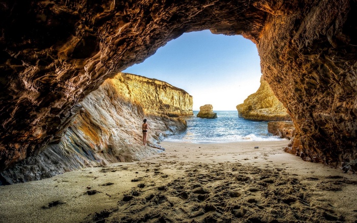 Woman standing on a beach inside a cave