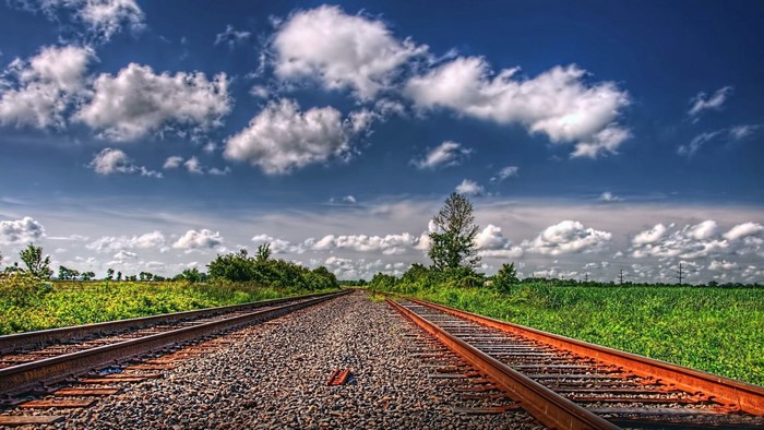 Railway tracks through a green landscape under a cloudy sky