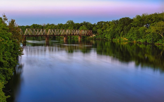 Rusty train bridge over a wide river at dusk