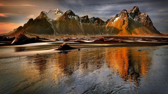 Rocky mountain range with snow-capped peaks reflected in a wet beach at sunset