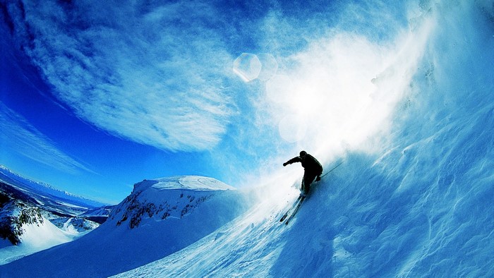 Skier skiing down a snowy mountain under a bright sky