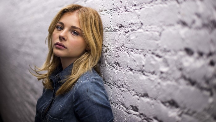 Chloe Moretz leaning against a brick wall