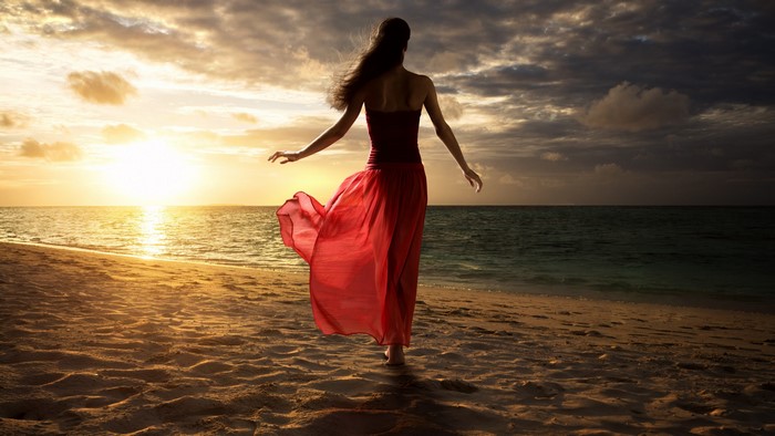 Woman in red dress on beach at sunset