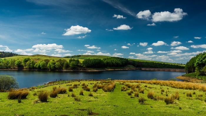 Green hills and lake under blue sky with clouds