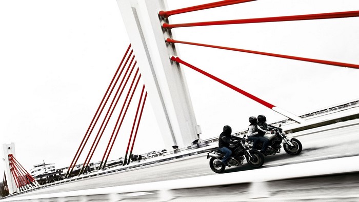 Motorcyclists on a bridge with red cables