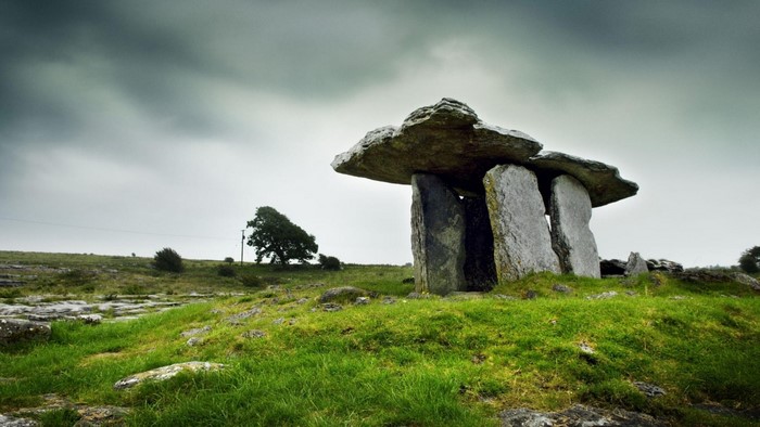 Ancient stone tomb in a grassy field under a cloudy sky