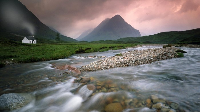 White cottage by a river with mountains