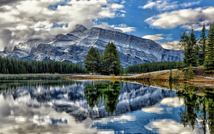 Mountain lake reflection with pine trees and clouds