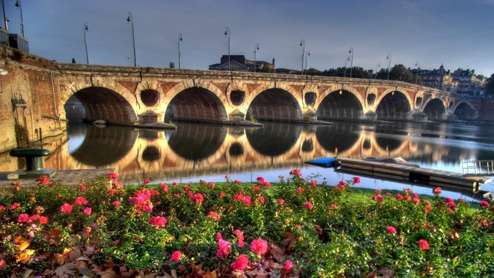 Stone bridge over a river with flowers in the foreground
