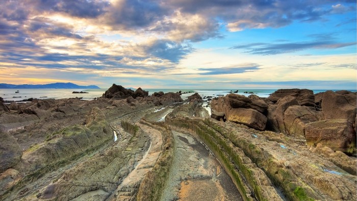 Rocky beach with layered rock formations and ocean under cloudy sky