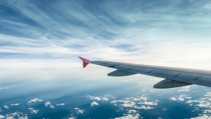 Airplane wing flying over clouds and ocean