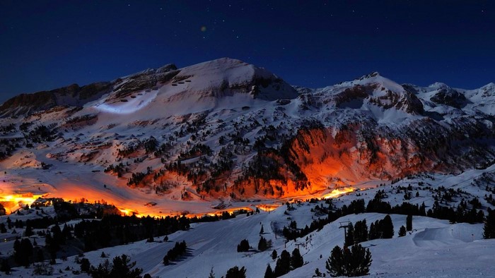 Snowy mountains illuminated by orange lights at night