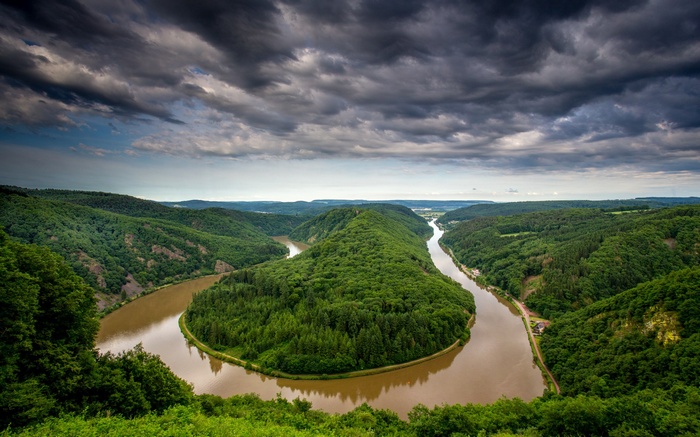 Meandering river through green forested hills under cloudy sky