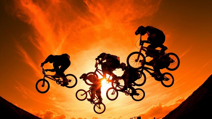 BMX riders performing stunts against a sunset