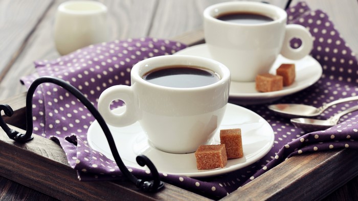 Two cups of coffee with sugar cubes on a tray
