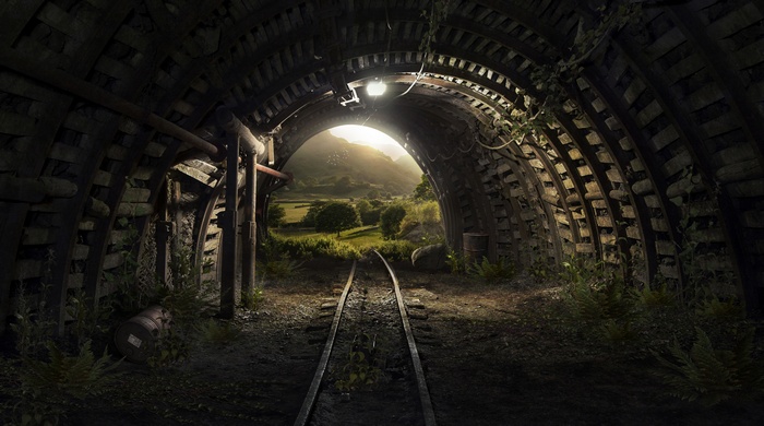 Tunnel with railway tracks leading to a sunlit landscape