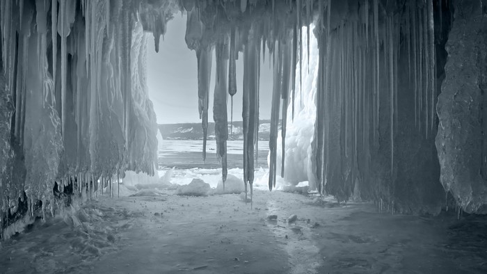 Ice cave with icicles and frozen lake view