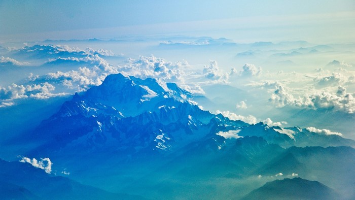 Snow-capped mountains above clouds from airplane