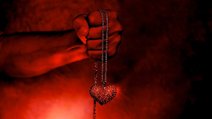 Fist holding a heart-shaped pendant necklace