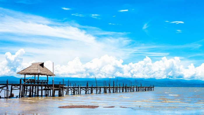Wooden pier with thatched hut on a lake under blue sky