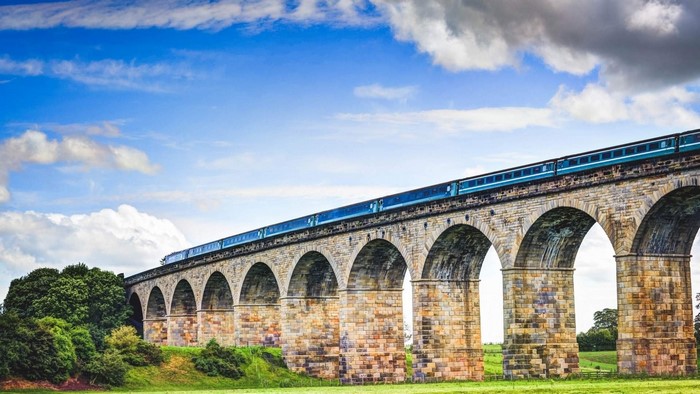 Train crossing a stone viaduct under a blue sky