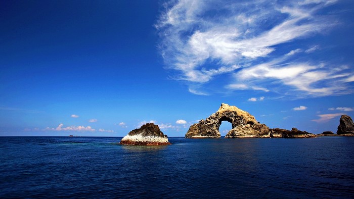 Arch rock formation in the ocean under a blue sky