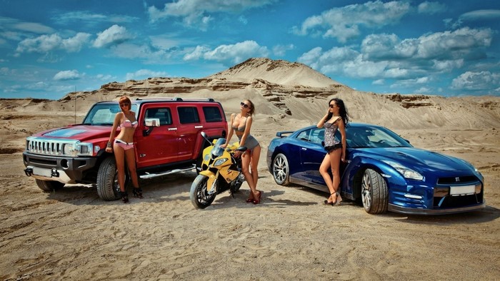 Three women with a red SUV, yellow motorcycle, and blue sports car in the desert.