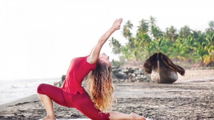 Woman in red performing yoga on a beach