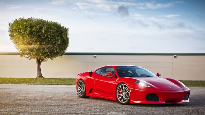 Red Ferrari F430 parked next to a tree