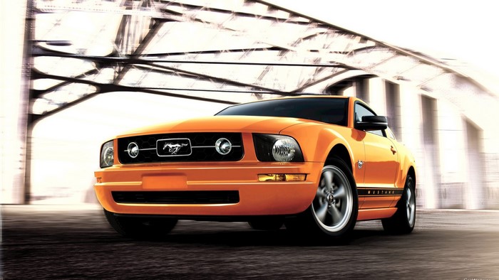 Orange Ford Mustang driving under a bridge