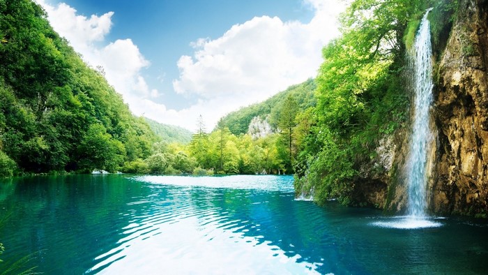 Waterfall landscape with turquoise lake and green forest