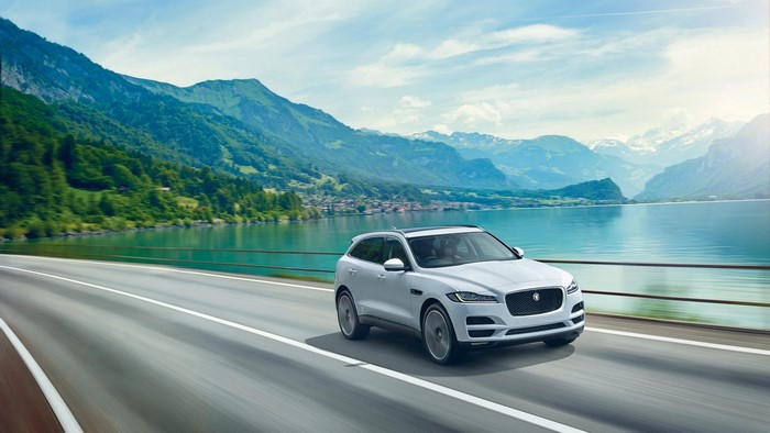 White Jaguar F-Pace driving on a road with mountains and lake